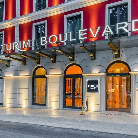 Turim Boulevard Hotel (Adults Only) Lisbona Esterno foto The image shows the exterior of a hotel named "Turim Boulevard." The building features a modern architectural design with a distinctive red facade and large arched windows. The hotel's name is prominently displayed in illuminated letters above the en