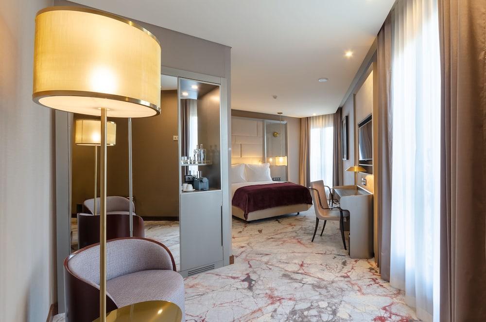 Turim Boulevard Hotel (Adults Only) Lisbona Esterno foto The photo depicts a modern hotel room featuring a sophisticated design. In the foreground, there is a stylish lamp next to a combination of seating areas: a plush armchair and a sleek chair beside a desk. The room has a king-sized bed, dressed in ele