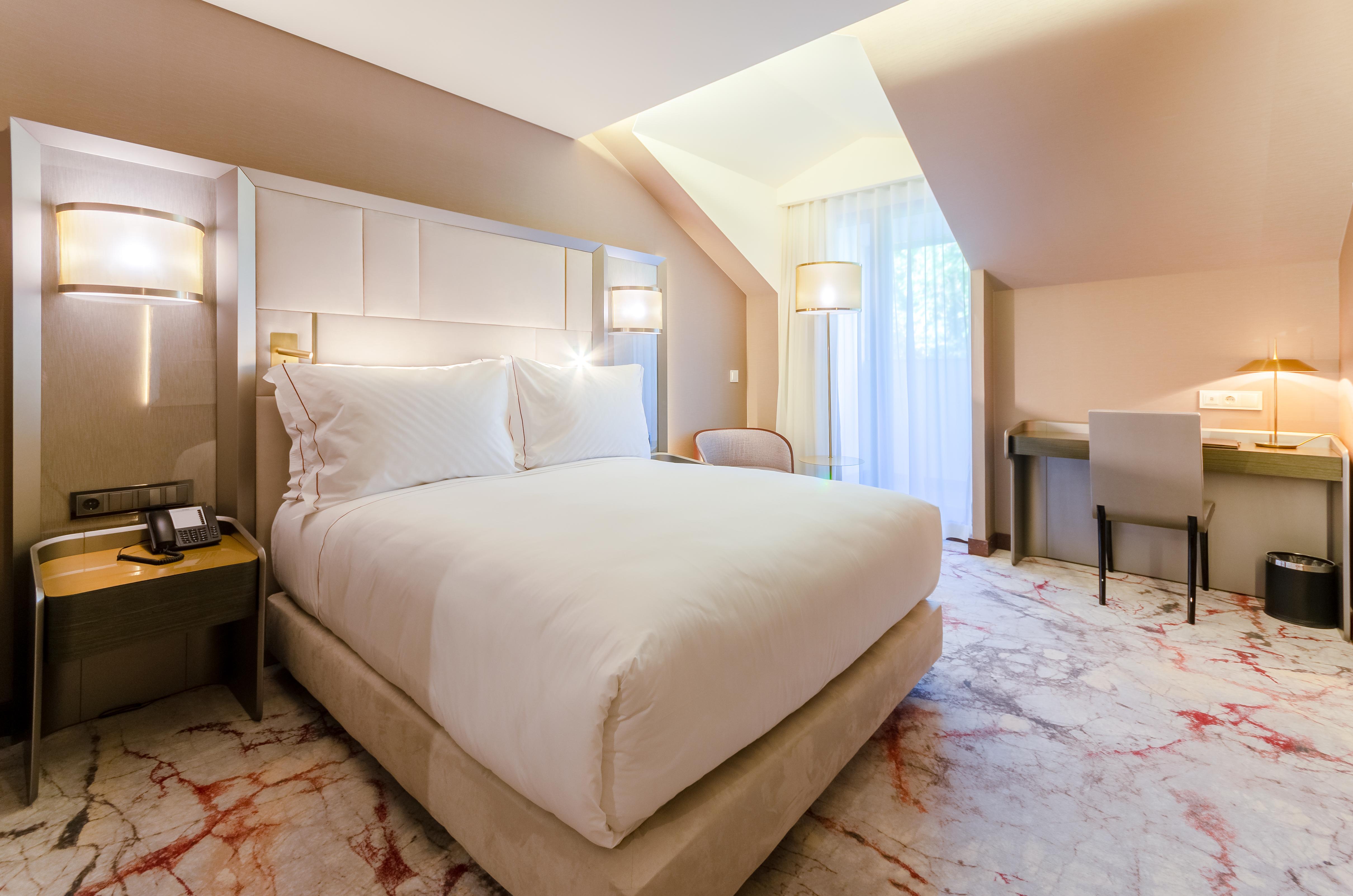 Turim Boulevard Hotel (Adults Only) Lisbona Esterno foto The photo shows a stylish hotel room featuring a large, comfortable bed with white linens. The room has a modern design with soft lighting, and there are bedside tables on either side of the bed. To one side, there's a cozy chair, and across from the