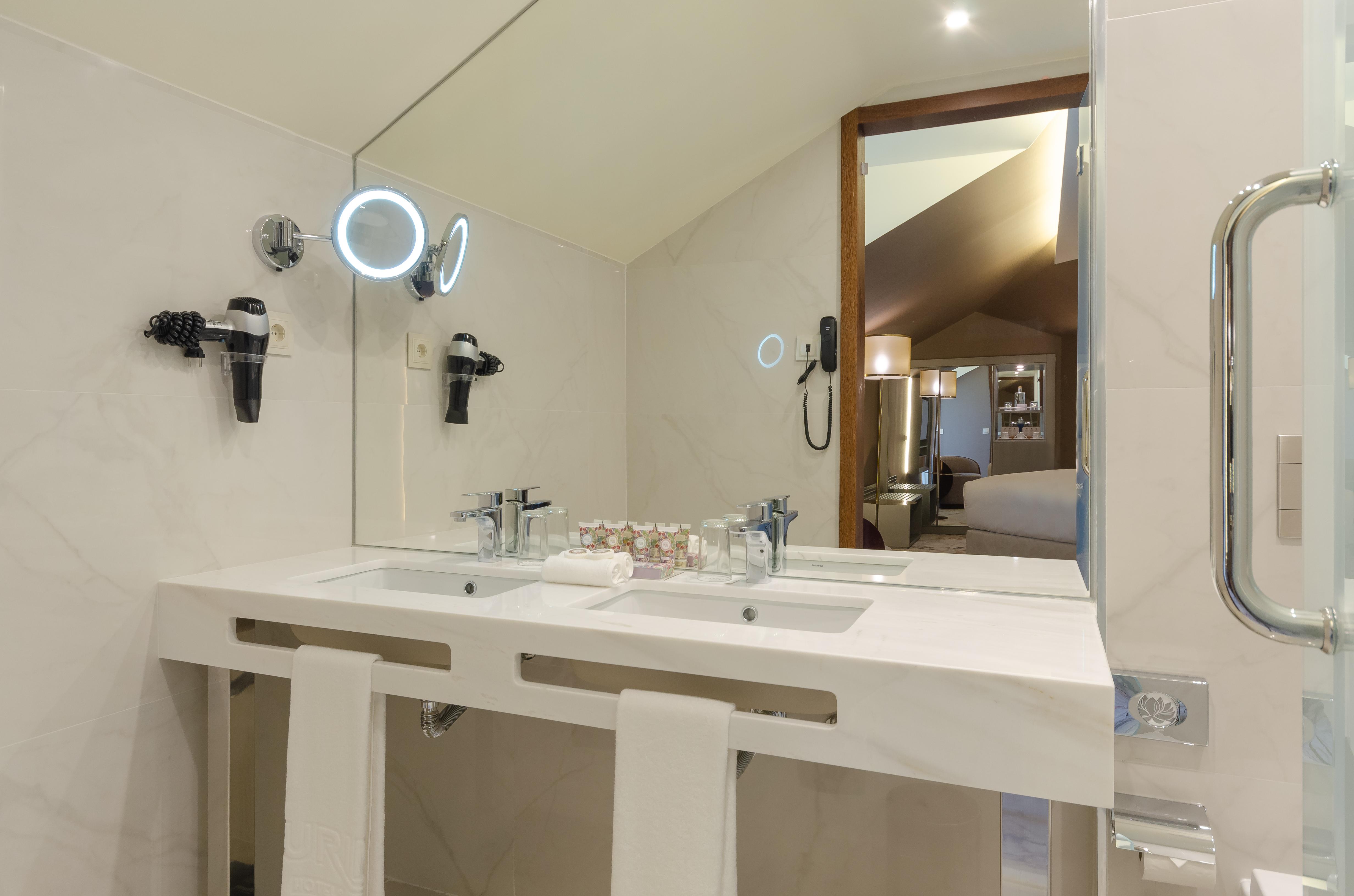 Turim Boulevard Hotel (Adults Only) Lisbona Esterno foto The photo shows a modern bathroom featuring a double sink with a white marble countertop. Above the sinks, there are stylish mirrors, one of which has an integrated LED light. The bathroom includes hair dryers mounted on the wall and a towel rack wit
