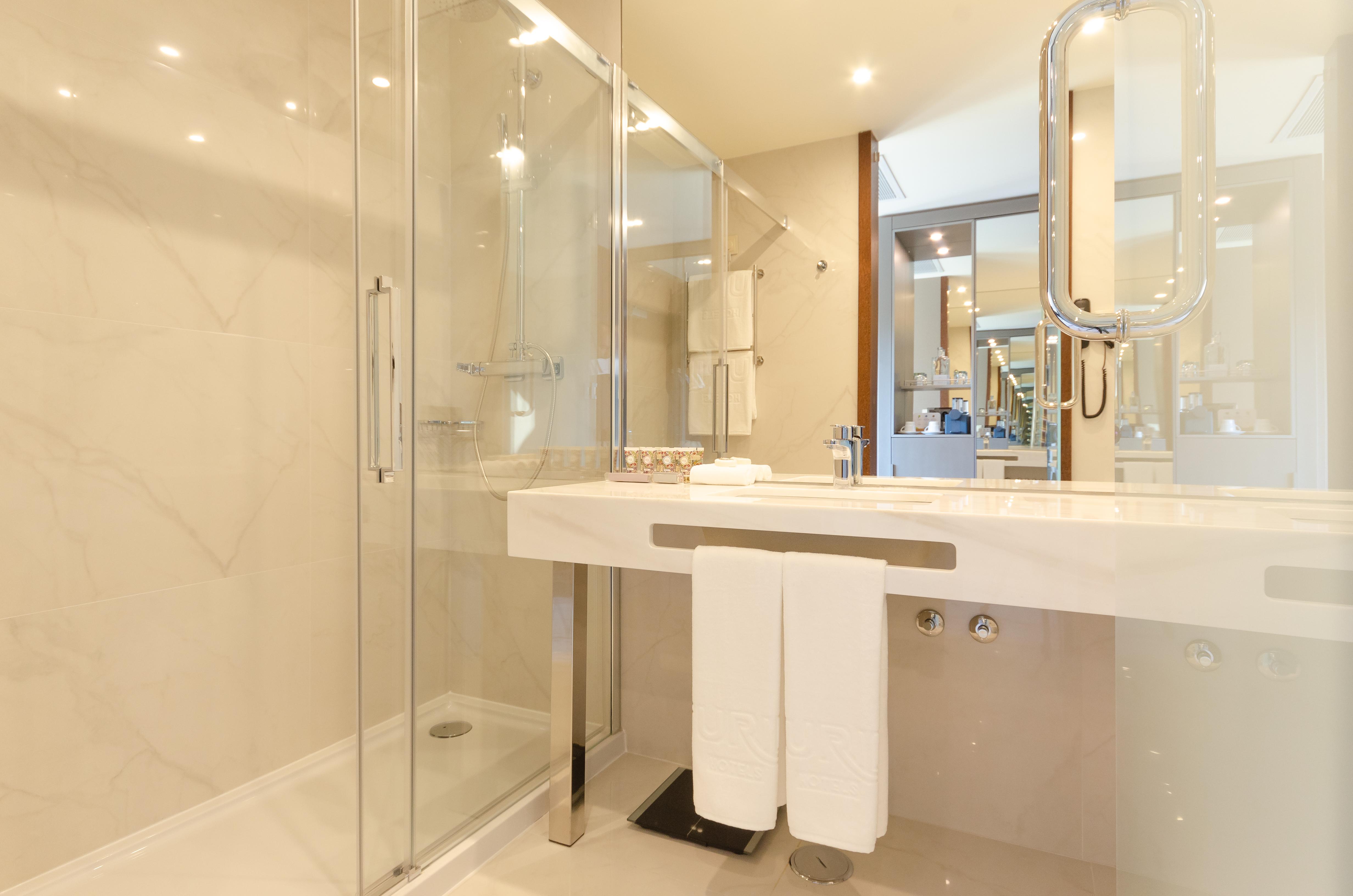 Turim Boulevard Hotel (Adults Only) Lisbona Esterno foto The photo shows a modern bathroom featuring a glass shower enclosure with a sleek design. There is a contemporary sink area with a large mirror above it. The countertop is minimalistic and has some toiletries neatly arranged. Two white towels hang fr