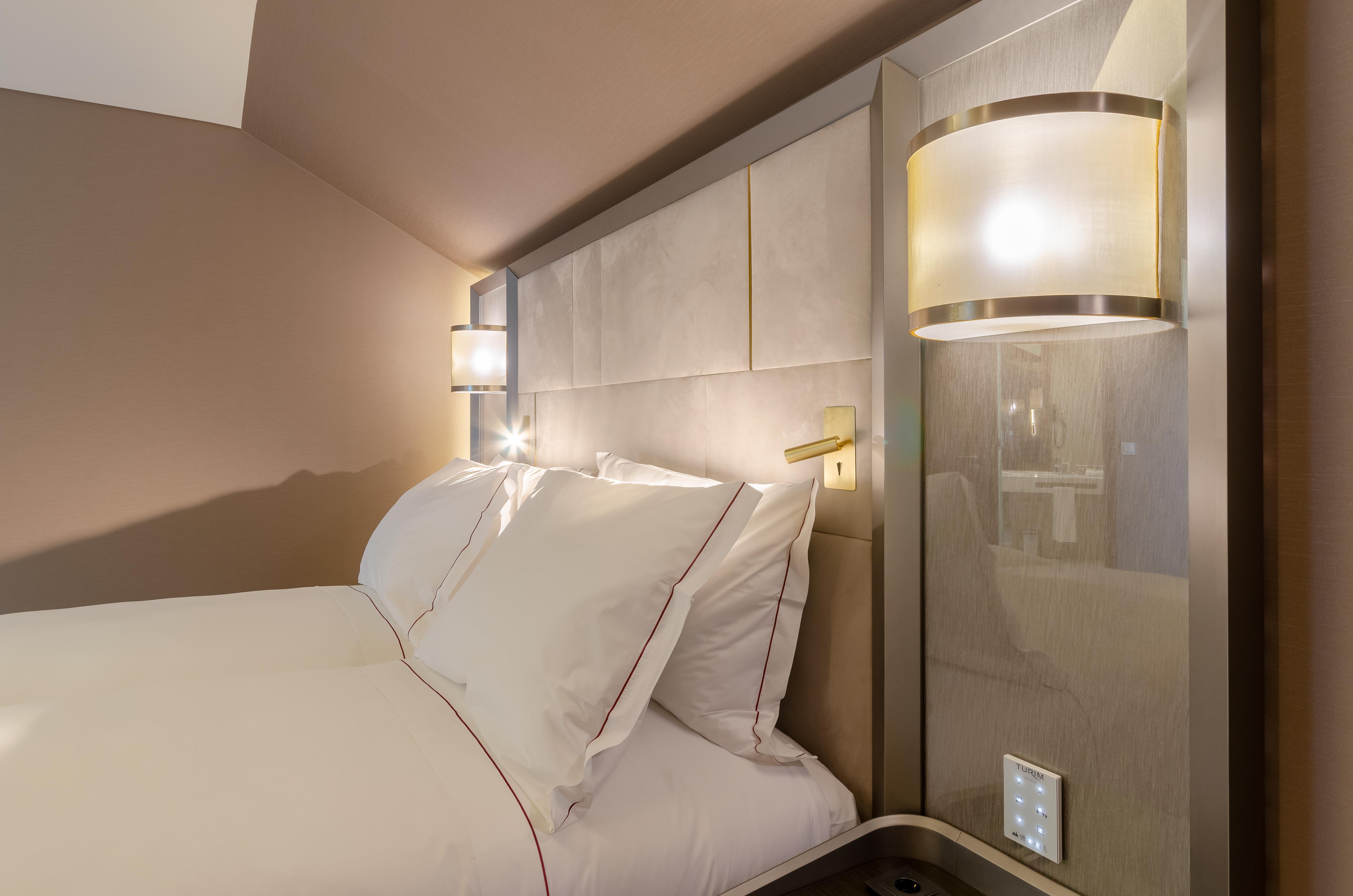 Turim Boulevard Hotel (Adults Only) Lisbona Esterno foto The photo shows a cozy hotel room with a neatly made bed featuring white bedding and decorative pillows. The headboard is upholstered and modern, with a light color scheme that includes gray and beige tones. On either side of the bed, there are styli