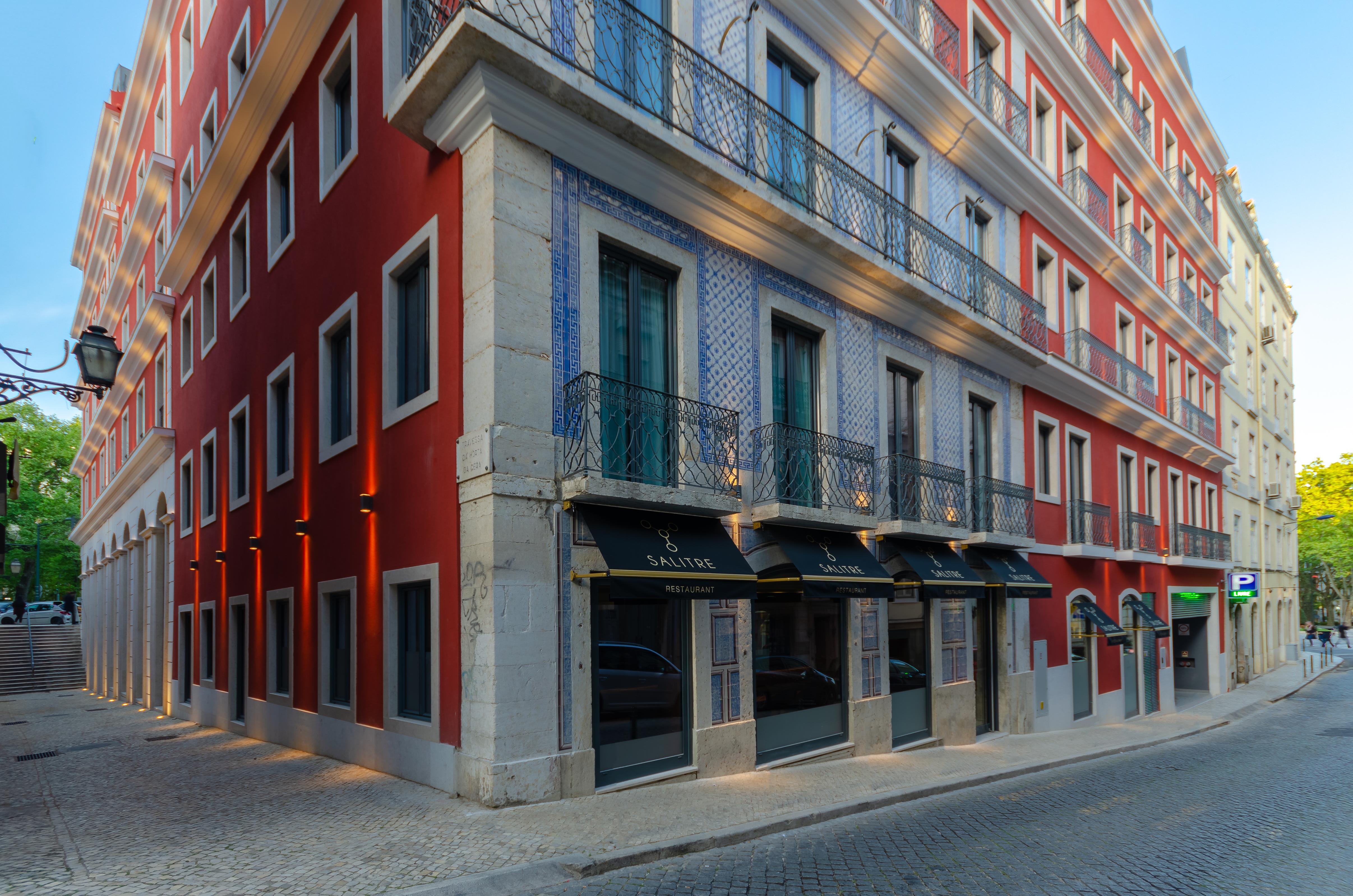 Turim Boulevard Hotel (Adults Only) Lisbona Esterno foto The photo shows a building with a striking architectural design, featuring a combination of red and blue facades. The corner of the building is highlighted, showcasing large windows with decorative railings. The ground floor appears to have storefron