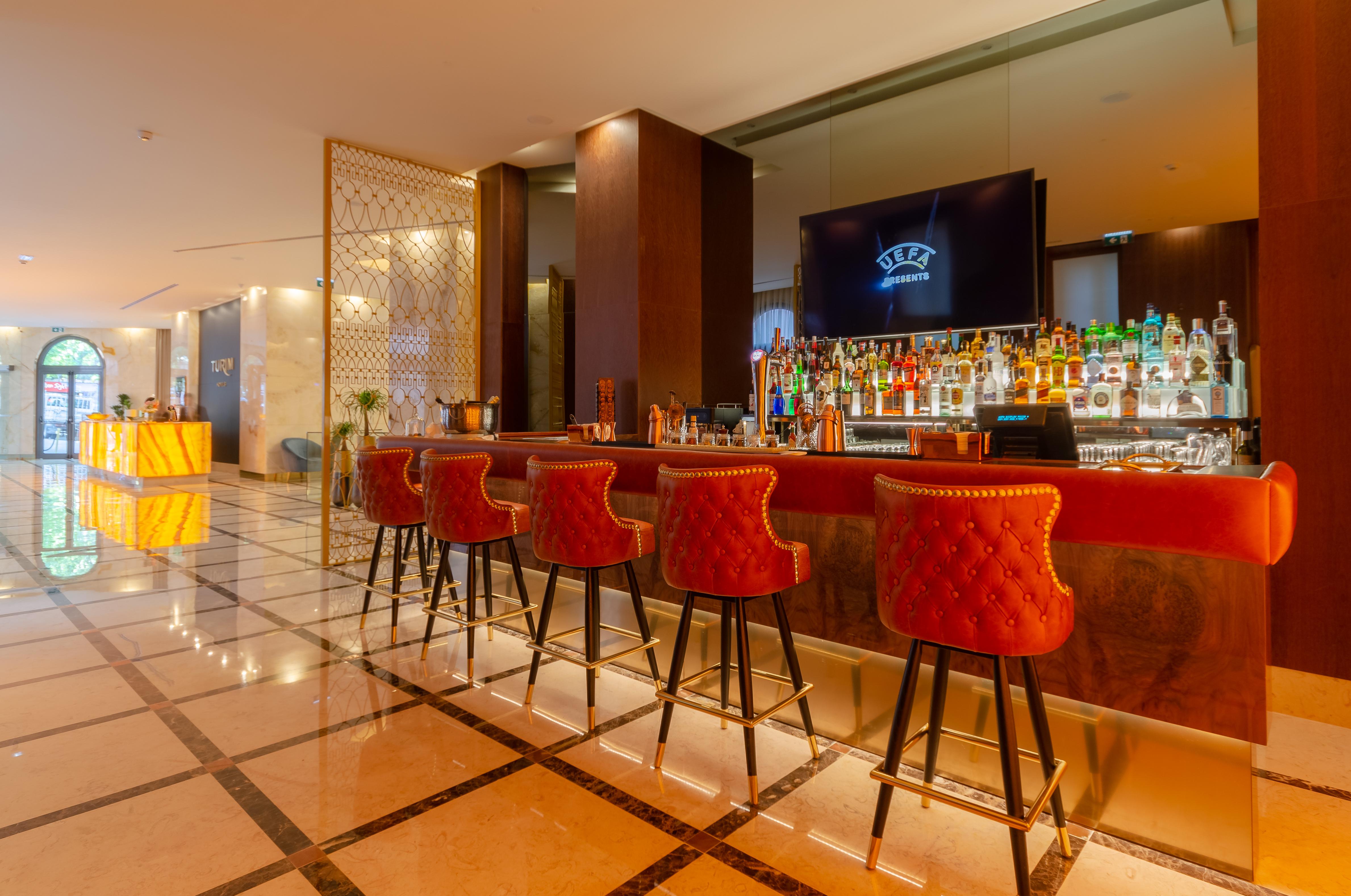 Turim Boulevard Hotel (Adults Only) Lisbona Esterno foto The photo shows a modern bar area with an elegant design. In the foreground, there are several high-backed red bar stools arranged in front of a stylish bar. The bar itself is well-stocked with a variety of bottles, indicating a selection of alcoholi