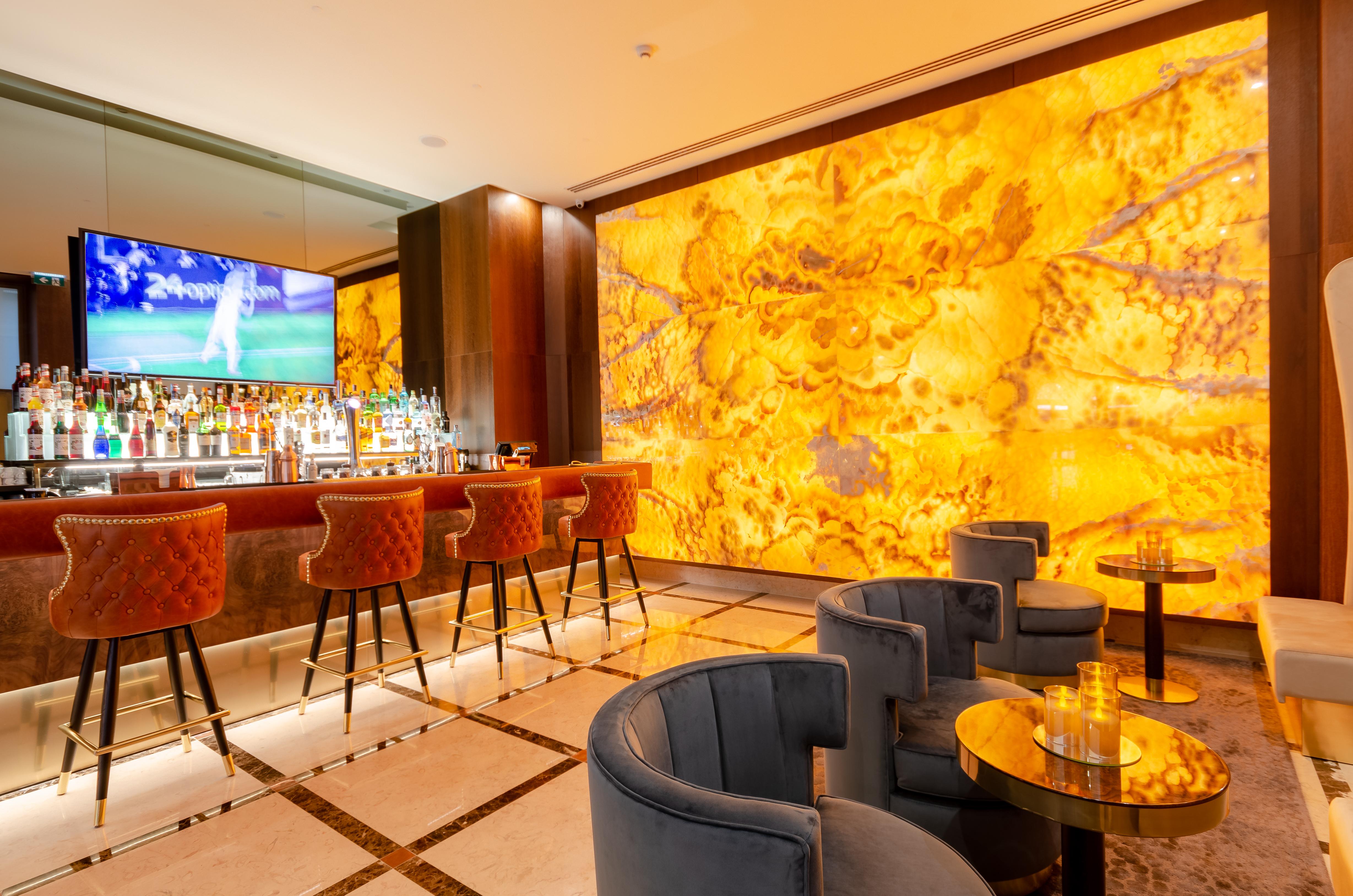 Turim Boulevard Hotel (Adults Only) Lisbona Esterno foto The photo shows a stylish bar area with a modern aesthetic. In the center, there is a well-stocked bar with an illuminated backdrop featuring a vibrant yellow wall, which appears to be made of a decorative stone or glass. The bar stools are upholster
