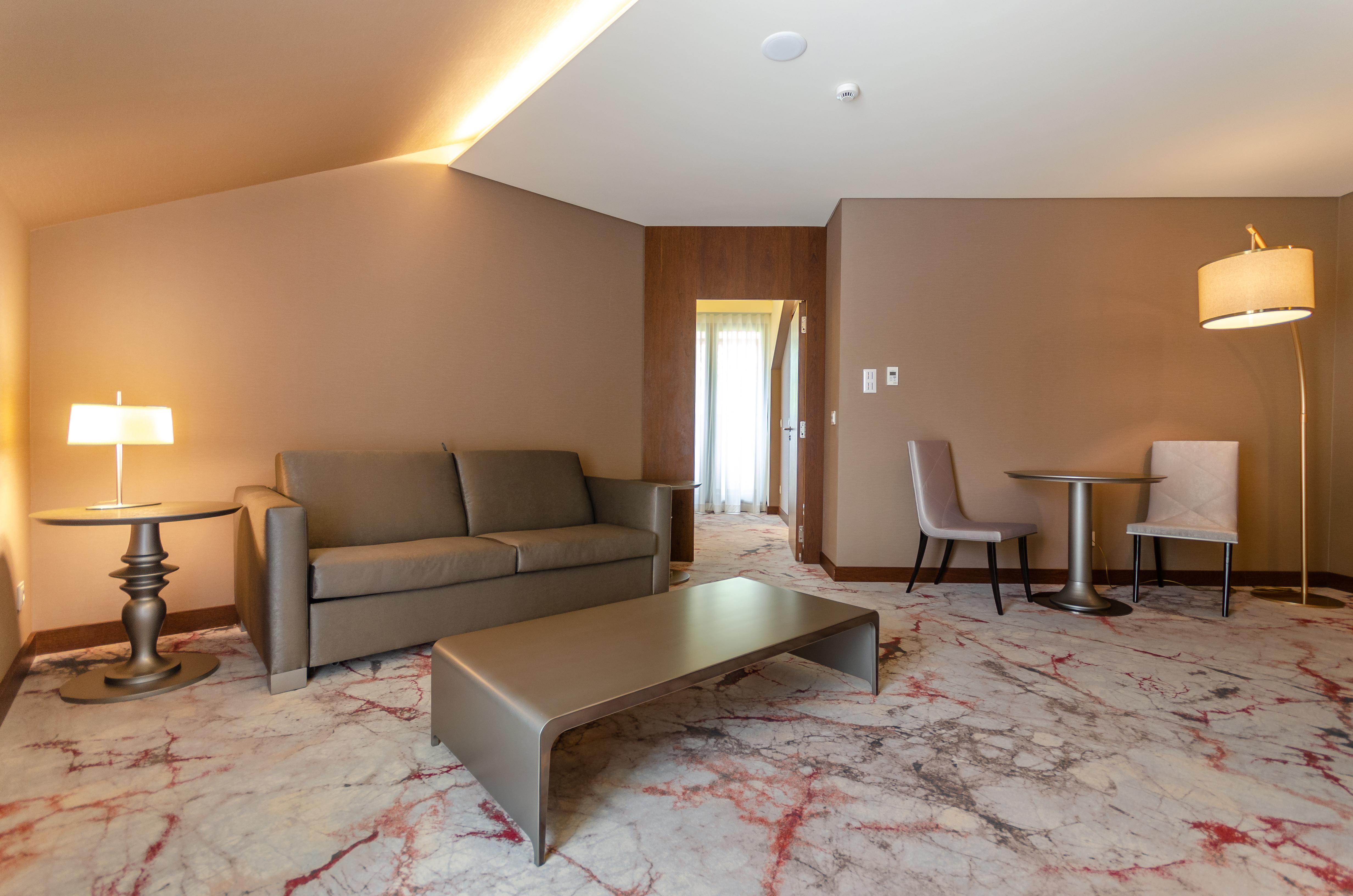 Turim Boulevard Hotel (Adults Only) Lisbona Esterno foto The photo shows a modern living space, likely part of a hotel suite or a stylish apartment. It features a light gray sofa positioned against a wall, accompanied by a small round table and two stylish chairs. A large coffee table with a sleek design s