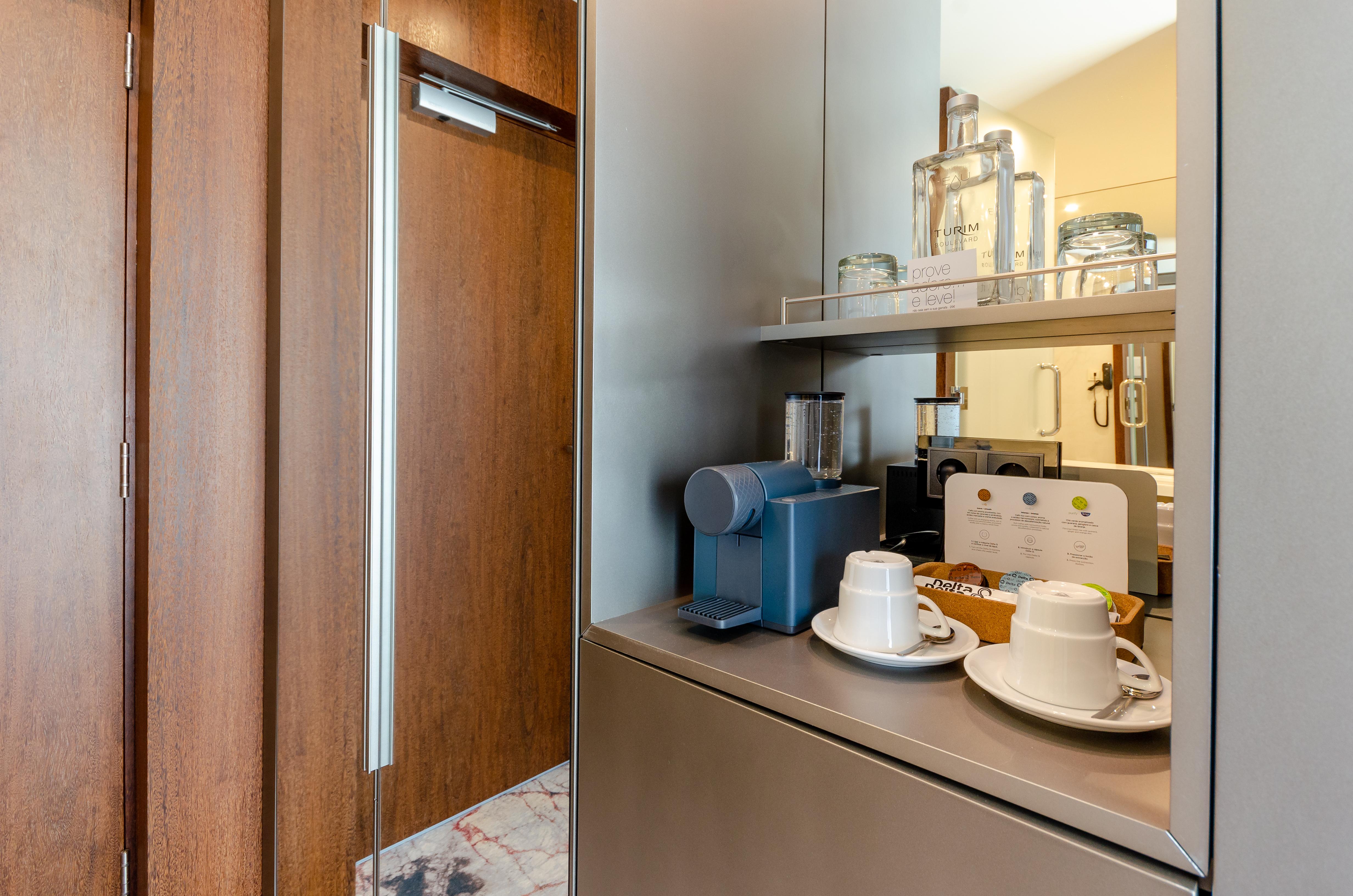 Turim Boulevard Hotel (Adults Only) Lisbona Esterno foto The photo shows a neatly organized area, likely within a hotel room or a modern kitchenette. On the left, there is a large wooden door, possibly a closet or entrance to another room. To the right, there is a stylish setup featuring a coffee maker in 