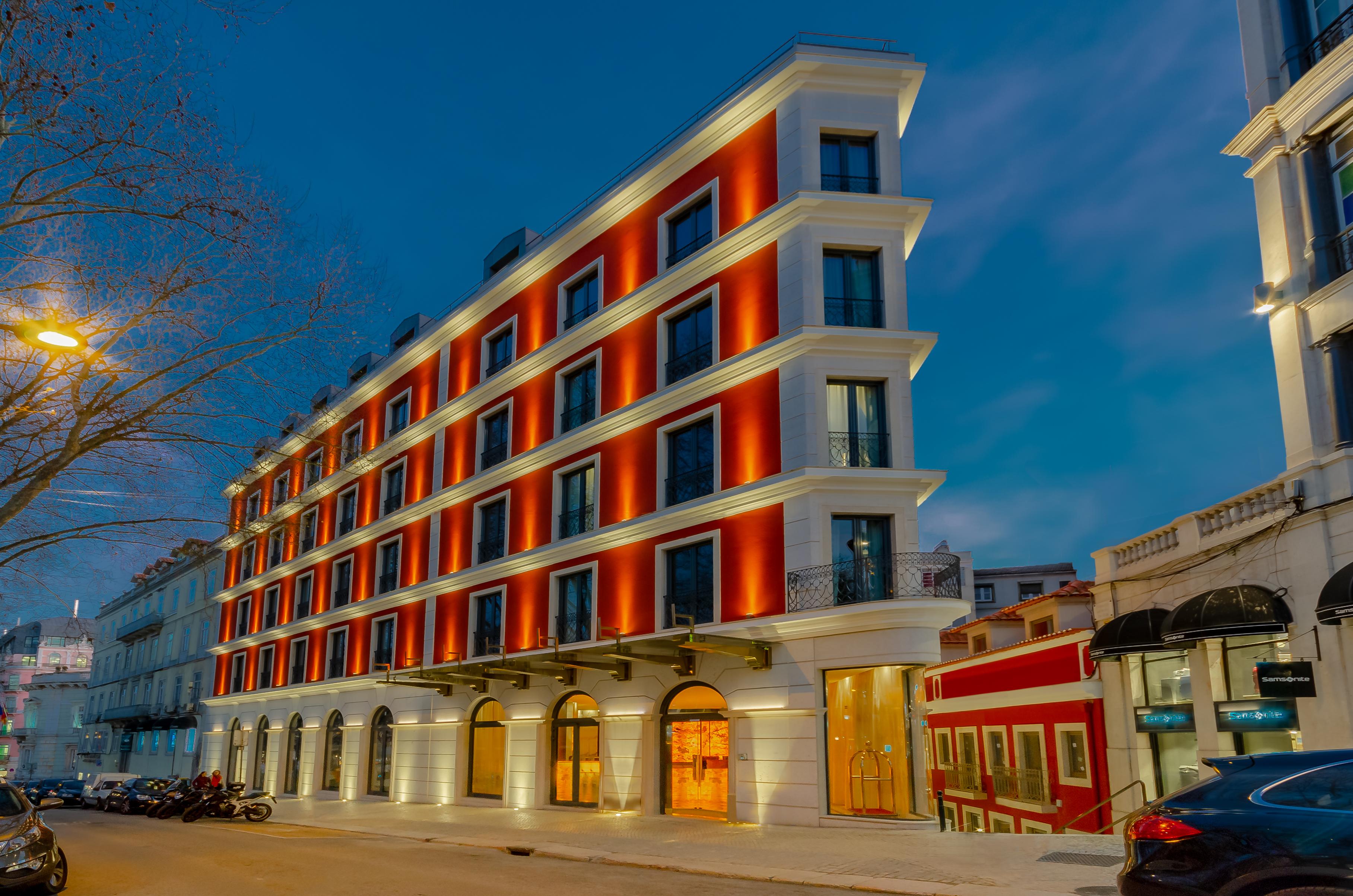 Turim Boulevard Hotel (Adults Only) Lisbona Esterno foto The photo shows a modern hotel building with a striking architectural design. The building features several floors with large windows, and it is illuminated by warm orange lights that create a welcoming ambiance. The facade has a contemporary style w