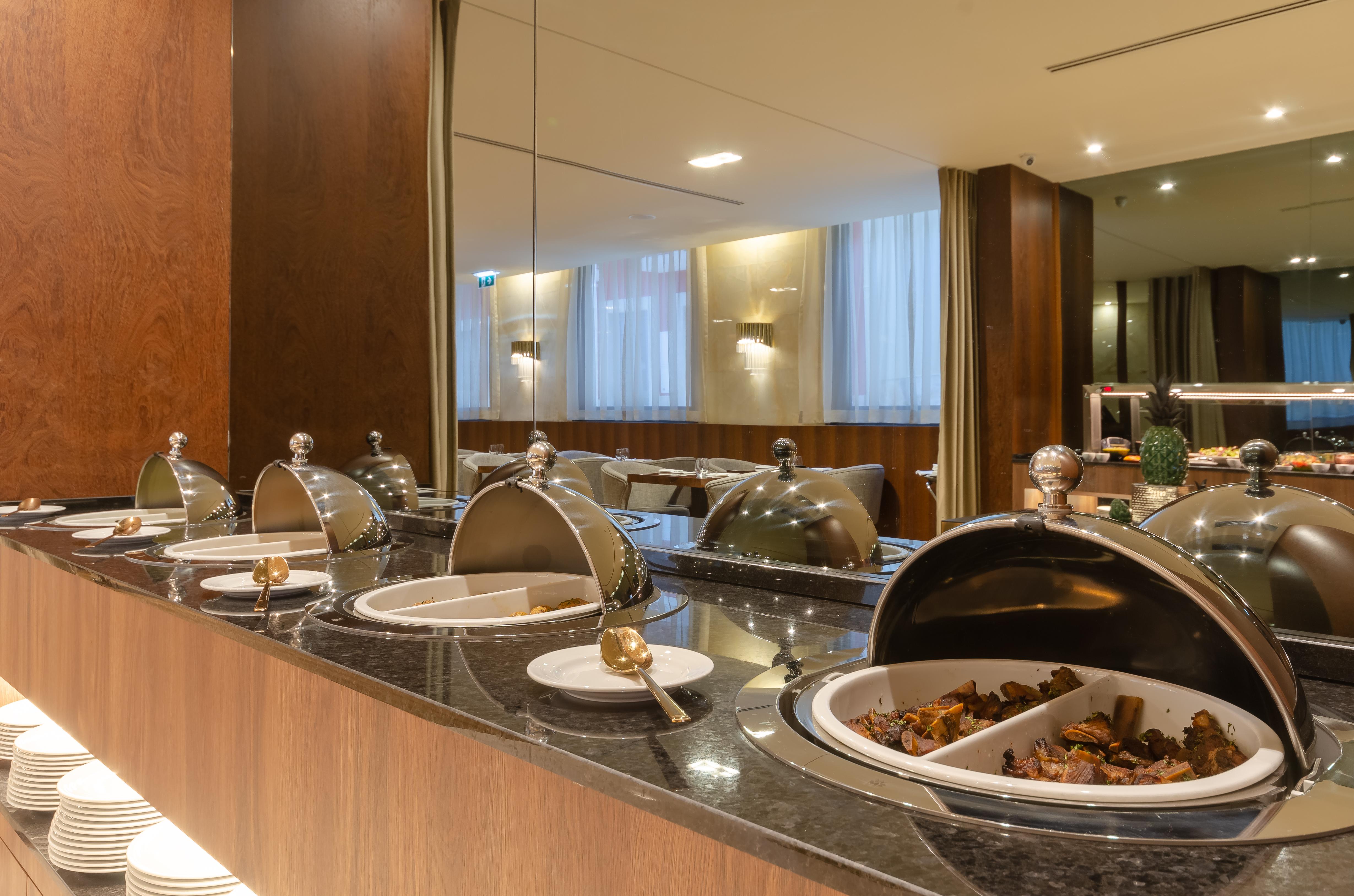 Turim Boulevard Hotel (Adults Only) Lisbona Esterno foto The photo shows a buffet setup in a dining area. There is a wooden counter with several covered food containers, which likely contain different dishes. The containers have shiny lids and are arranged neatly along the counter. One of the containers is