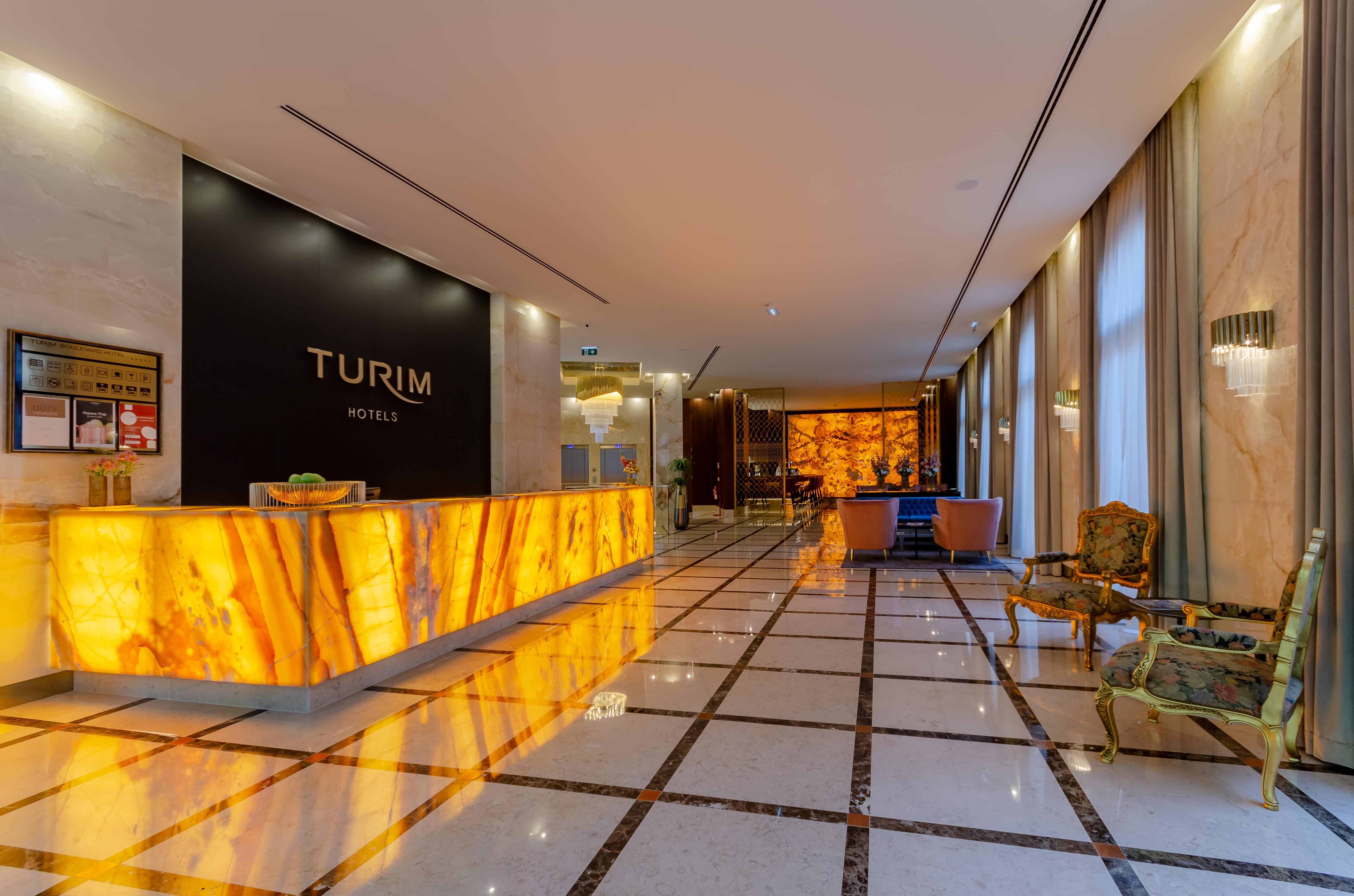 Turim Boulevard Hotel (Adults Only) Lisbona Esterno foto The image shows the interior of a hotel lobby. The design features a modern and elegant style, with a prominent reception desk illuminated by warm lighting, likely made of stone or a similar material, displaying the name "TURIM HOTELS" prominently. T