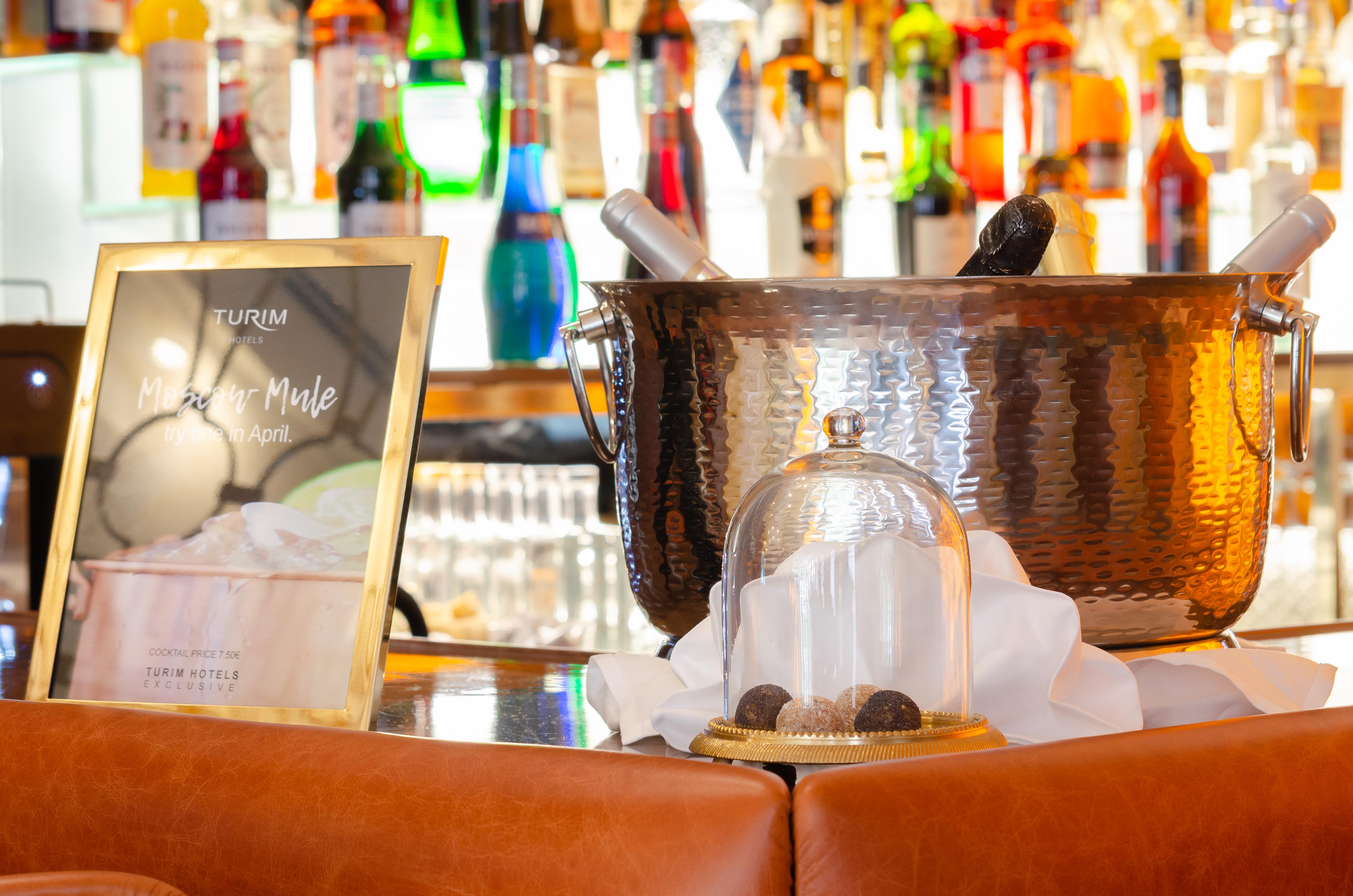 Turim Boulevard Hotel (Adults Only) Lisbona Esterno foto The photo depicts a bar setting. In the foreground, there is a vintage-style silver bucket, likely used for chilling drinks, surrounded by a white cloth. There is also a small cloche covering a plate of chocolates or truffles on a decorative gold tra