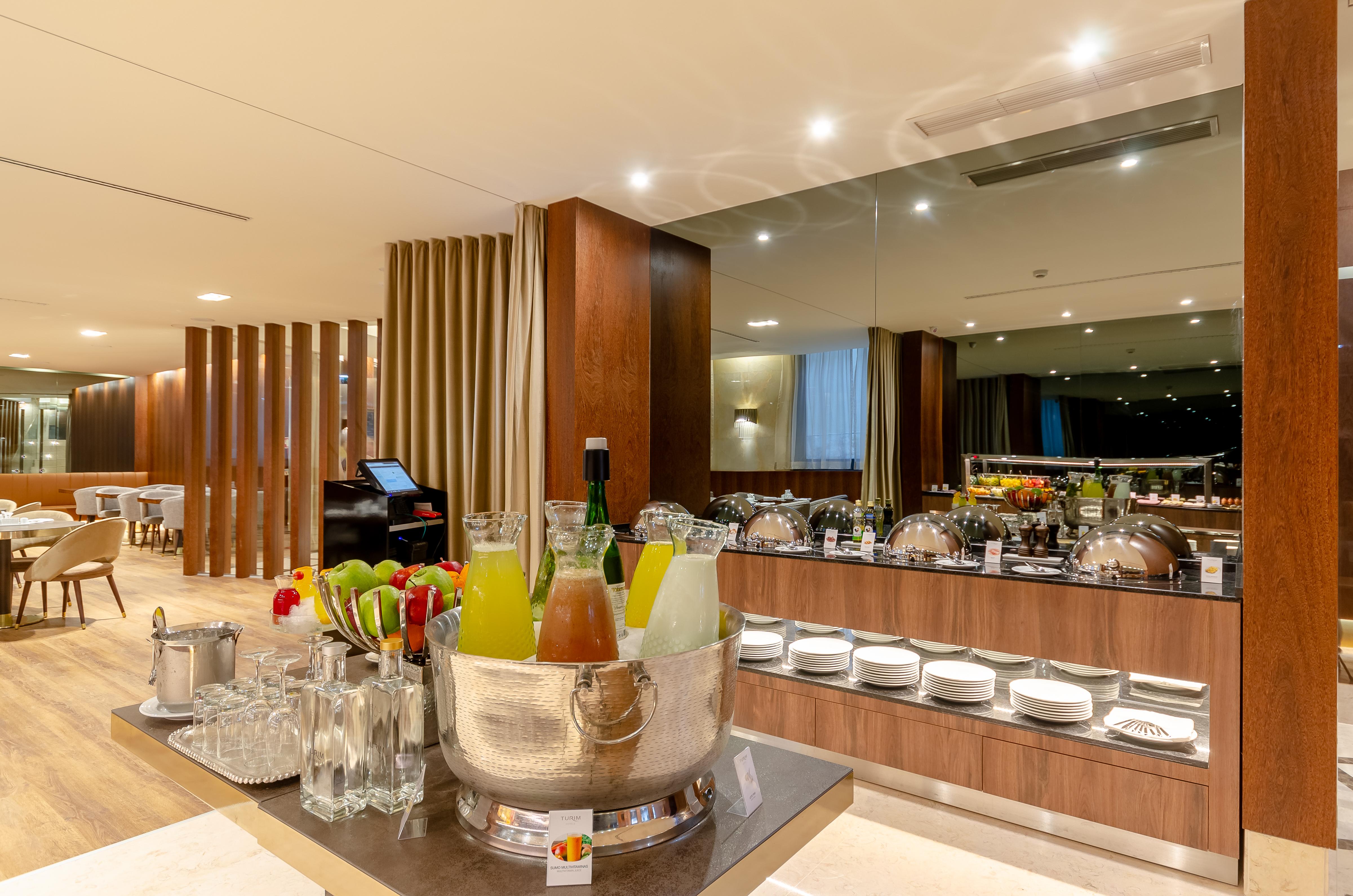 Turim Boulevard Hotel (Adults Only) Lisbona Esterno foto The photo shows a modern dining area, likely in a hotel or restaurant setting. In the foreground, there is a large silver ice bucket filled with various beverages, including champagne and colorful cocktails or juices. Behind this, there is a buffet s
