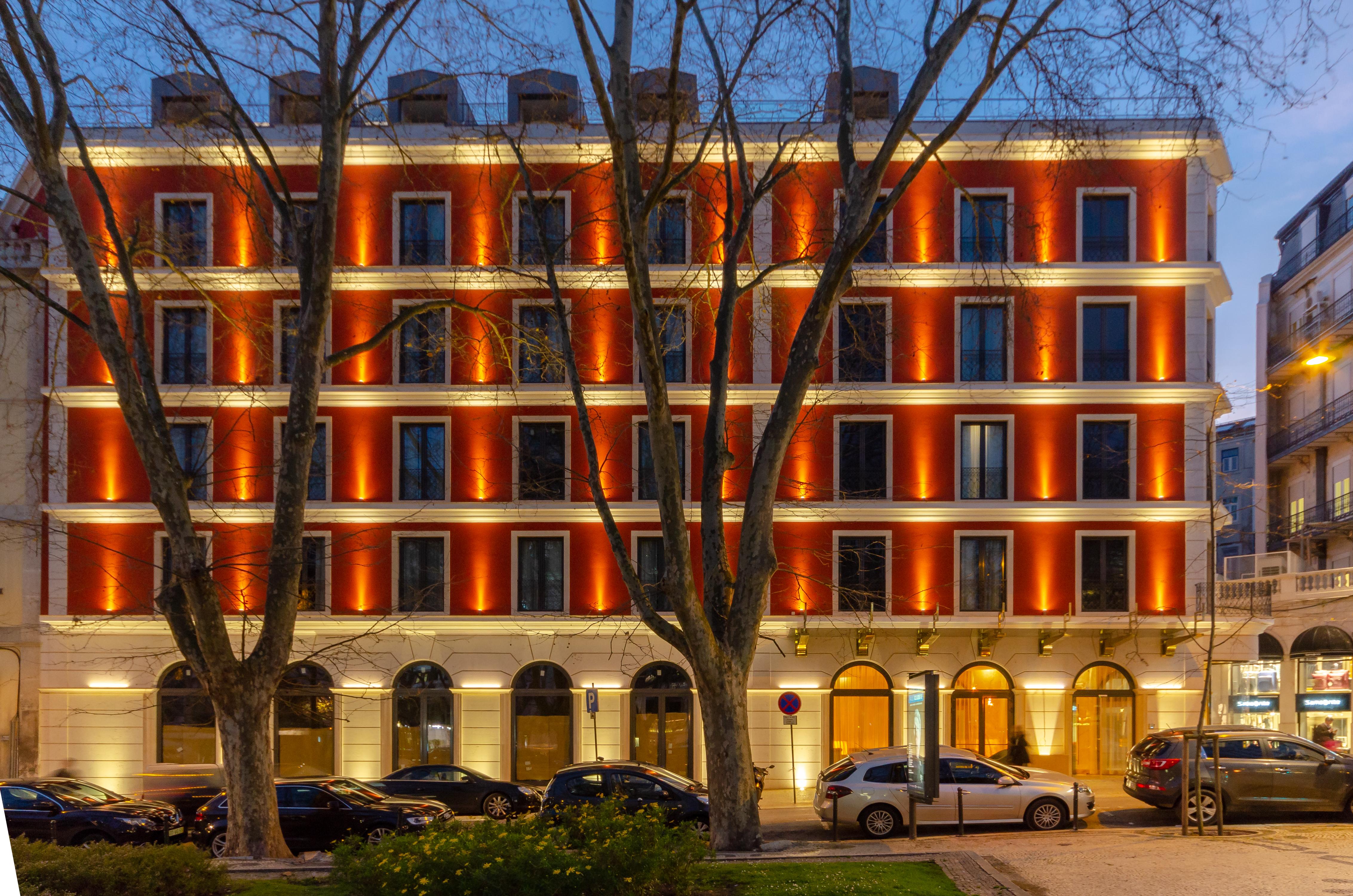 Turim Boulevard Hotel (Adults Only) Lisbona Esterno foto The photo shows a beautifully illuminated hotel building at dusk. The facade features a grid of windows with warm orange and white lighting that highlights the architectural details. There are several trees in front of the building, and a line of car