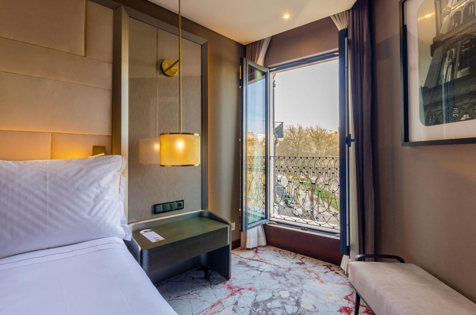 Turim Boulevard Hotel (Adults Only) Lisbona Esterno foto The photo depicts a modern hotel room featuring a comfortable bed with crisp white linens. There’s a small table beside the bed, and a stylish lamp hanging from the ceiling. The room has large windows that open to a view outside, allowing natural lig