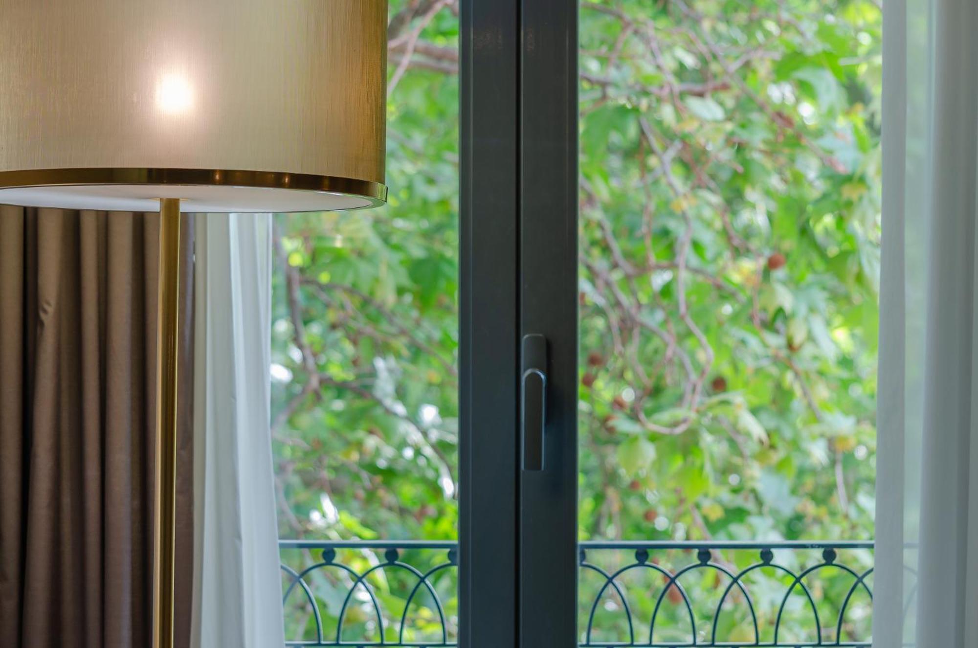 Turim Boulevard Hotel (Adults Only) Lisbona Esterno foto The photo shows a window with a modern design, featuring a dark frame and a handle for opening. To one side, there is a pendant lamp with a light shade that has a golden finish. The view outside the window reveals a lush green area, likely a garden o