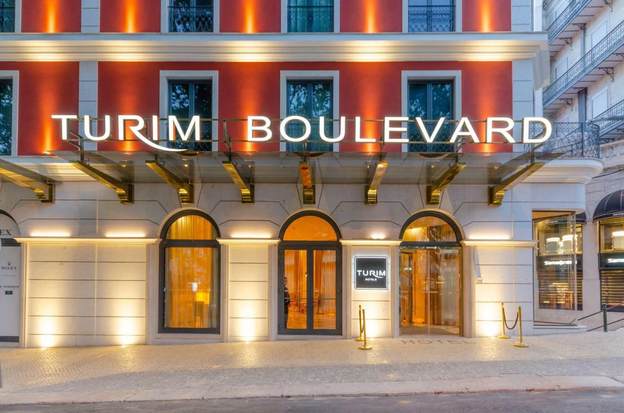 Turim Boulevard Hotel (Adults Only) Lisbona Esterno foto The photo shows the exterior of a hotel named "Turim Boulevard." The building features a modern architectural design with a combination of red and white colors. The entrance is marked by large arched windows and a glass canopy supported by metallic s