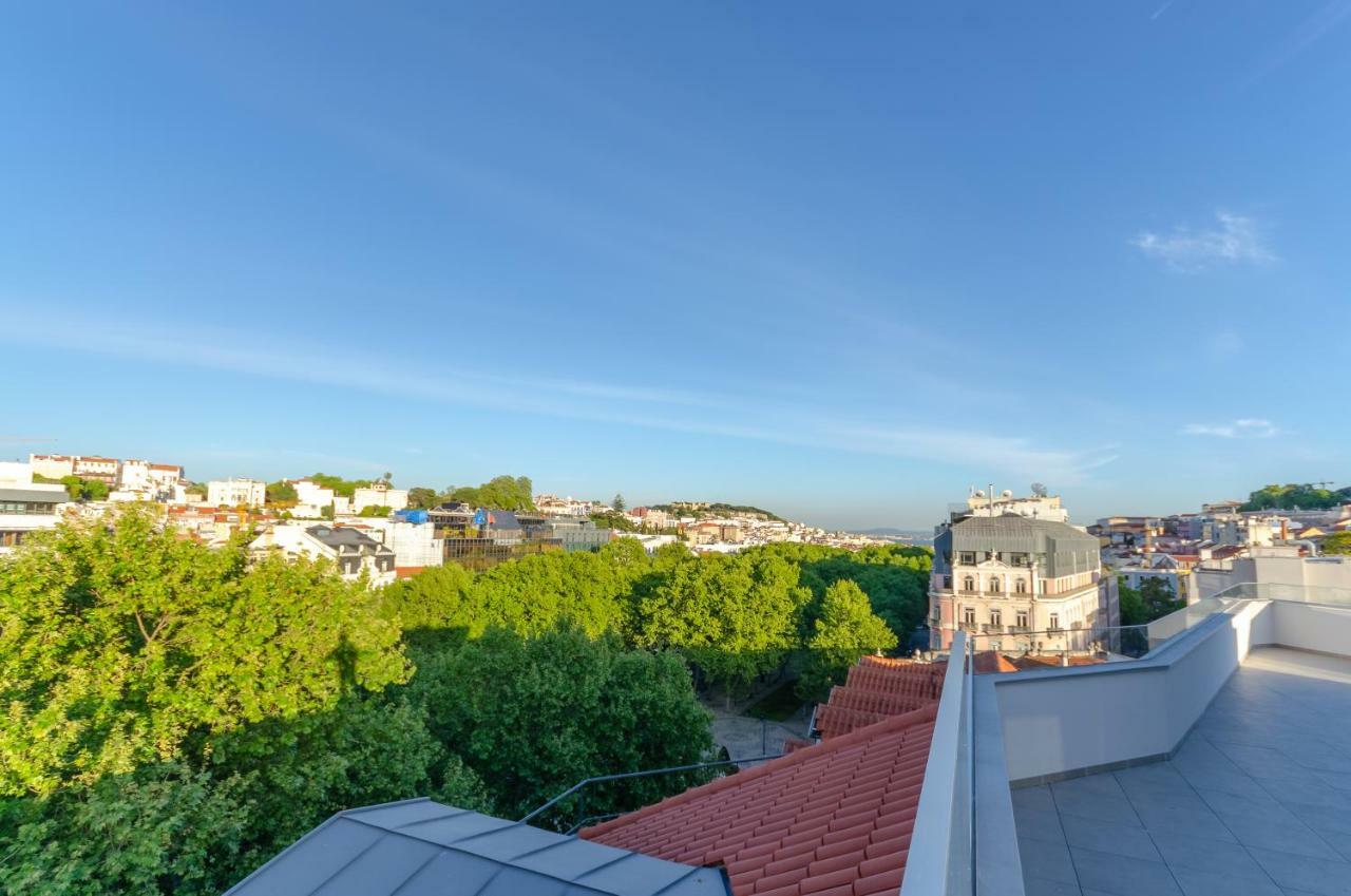 Turim Boulevard Hotel (Adults Only) Lisbona Esterno foto The photo shows a panoramic view of a cityscape with a mix of buildings and greenery. There are rooftops visible, with some areas covered in trees, indicating a park or green space nearby. The sky is clear with a bright blue hue, suggesting a sunny d
