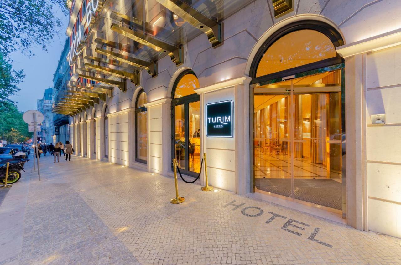 Turim Boulevard Hotel (Adults Only) Lisbona Esterno foto The photo shows the entrance of a hotel named "Turim Hotel." The exterior features elegant architecture with large arched windows and a modern design. Golden accents are visible on the entryway, and a red carpet is placed outside, suggesting a welcom