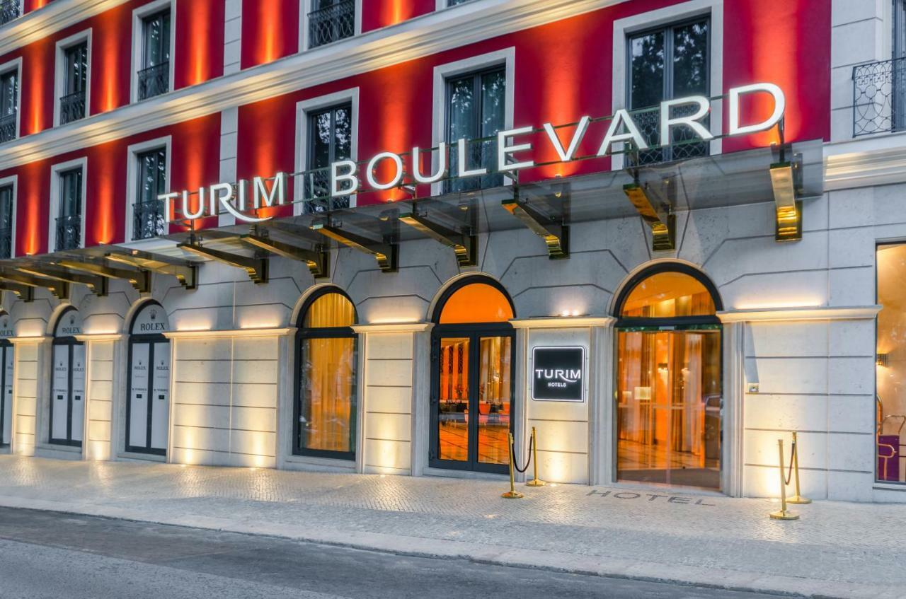 Turim Boulevard Hotel (Adults Only) Lisbona Esterno foto The image shows the exterior of a hotel named "Turim Boulevard." The building features a modern architectural design with a distinctive red facade and large arched windows. The hotel's name is prominently displayed in illuminated letters above the en