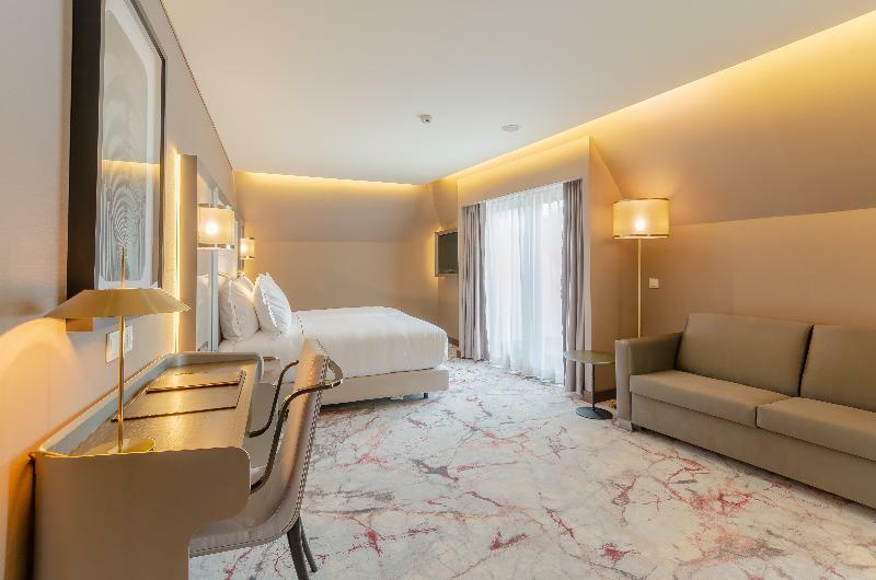Turim Boulevard Hotel (Adults Only) Lisbona Esterno foto The photo shows a modern hotel room featuring a spacious layout. There’s a large bed with plush white bedding, positioned against a light-colored wall. To one side, there's a small sitting area with a beige sofa. A stylish desk is also visible, with 