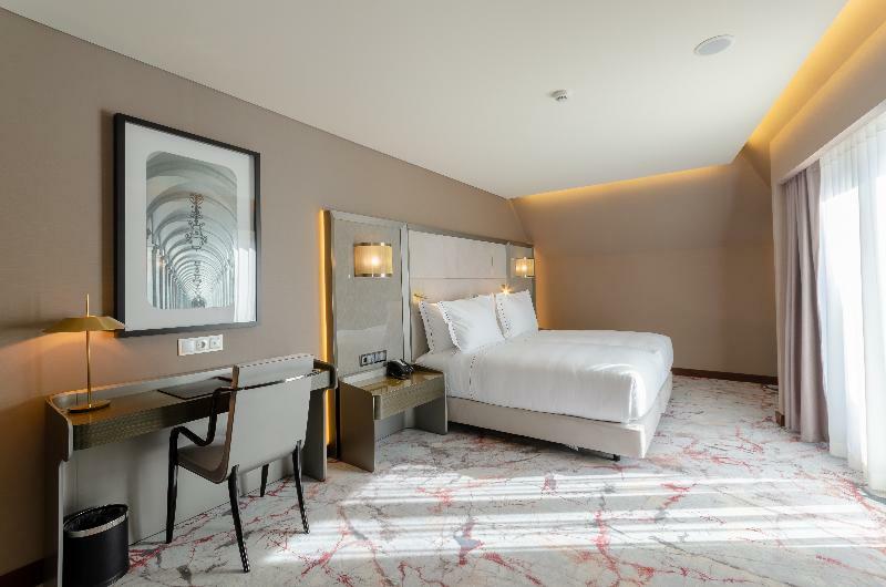 Turim Boulevard Hotel (Adults Only) Lisbona Esterno foto The photo shows a modern hotel room featuring a large bed with white bedding positioned against a light-colored wall. There is a minimalist desk and chair set up next to the bed, along with a lamp on the desk. The flooring appears to have a marbled d
