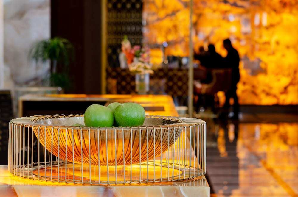Turim Boulevard Hotel (Adults Only) Lisbona Esterno foto The photo shows a decorative arrangement in a lobby or reception area. In the foreground, there is a wire bowl containing three green apples, placed on a surface that has a warm, illuminated glow. In the background, there are blurred silhouettes of p