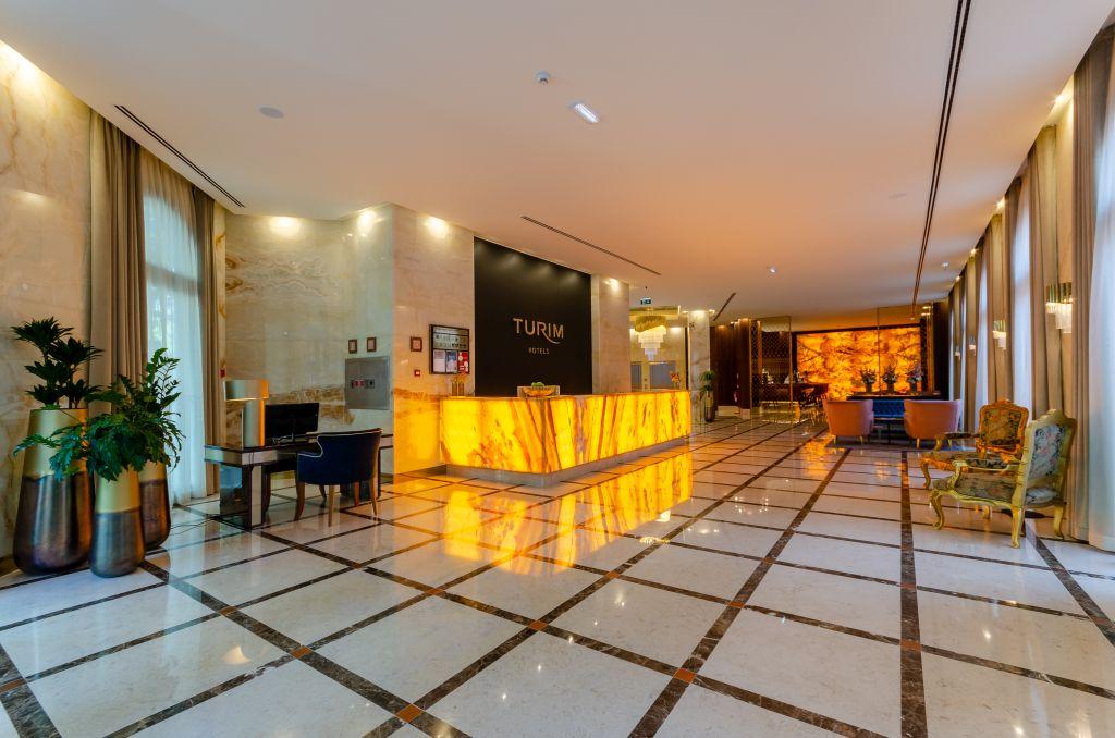 Turim Boulevard Hotel (Adults Only) Lisbona Esterno foto The image shows a modern hotel lobby with a sleek design. In the foreground, there is a polished marble floor with geometric patterns. The reception desk features a striking golden-hued counter that adds elegance to the space. Behind the desk, there’